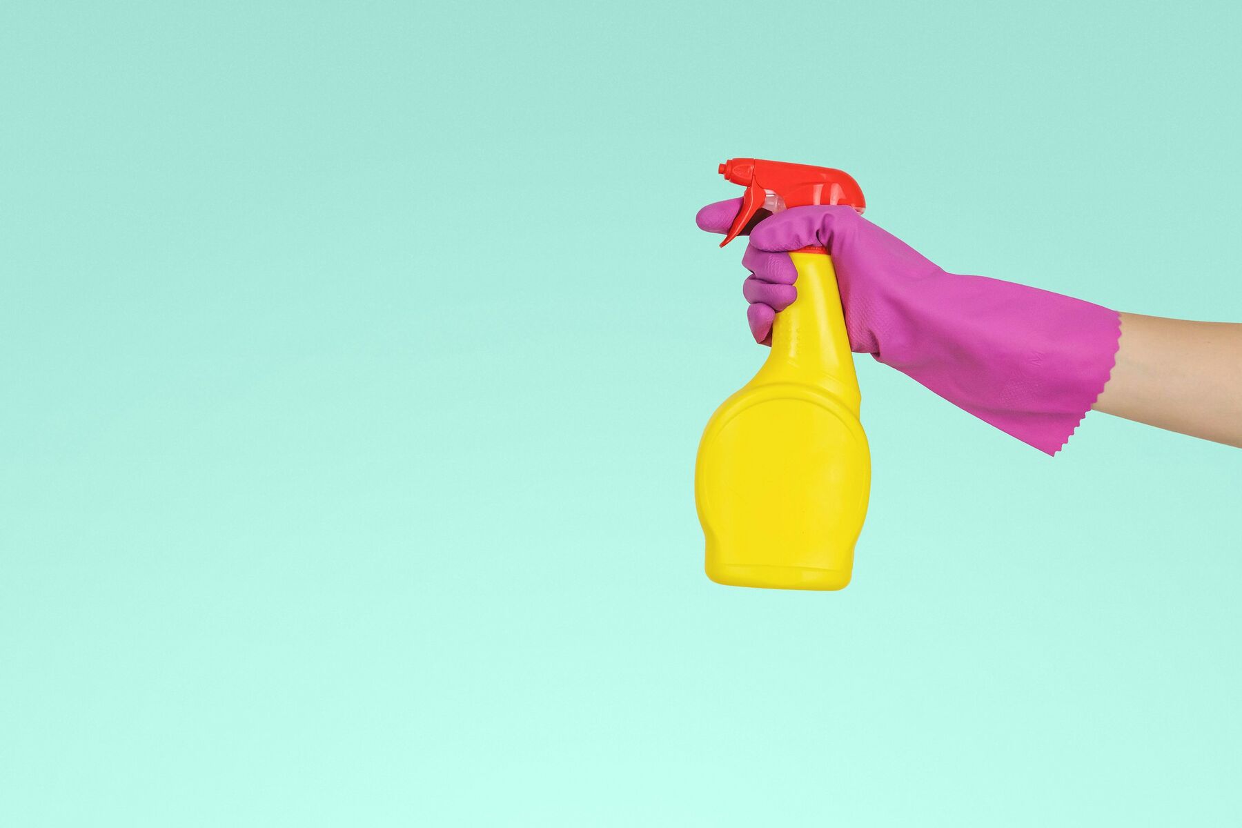 Gloved hand holding a cleaning spray bottle against a pale teal wall