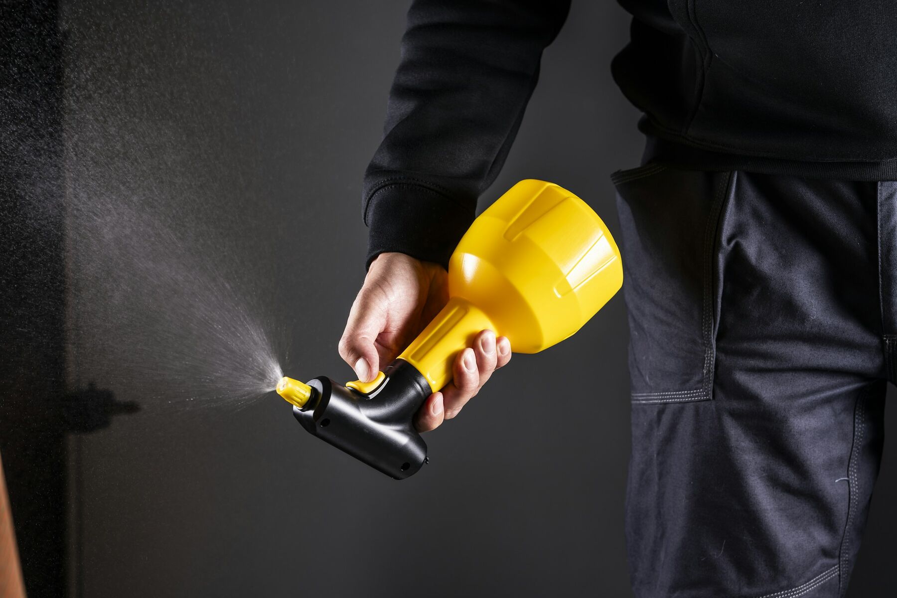 Technician in dark workwear holding a handheld pest treatment sprayer
